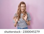Small photo of Beautiful blonde woman standing over pink background disgusted expression, displeased and fearful doing disgust face because aversion reaction.