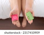 Young beautiful woman holding birth control pills and condom at bedroom