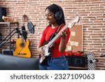 Young african american woman artist singing song playing electrical guitar at music studio