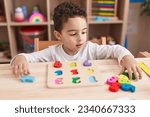 Small photo of Adorable hispanic boy playing with maths puzzle game sitting on table at kindergarten