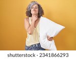Middle age woman with grey hair wearing pijama hugging pillow touching painful neck, sore throat for flu, clod and infection 