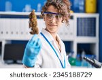 Young hispanic woman scientist smiling confident holding marihuana plant at laboratory