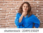Beautiful brunette woman standing over bricks wall touching painful neck, sore throat for flu, clod and infection 
