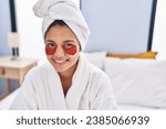 Small photo of Young latin woman having baggy eyes treatment sitting on bed at bedroom