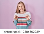 Small photo of Young blonde woman standing over pink background disgusted expression, displeased and fearful doing disgust face because aversion reaction.