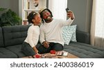 Small photo of African american father and daughter wearing king crown and baggy eyes pad make selfie by smartphone at home