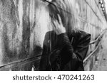 Small photo of Young woman suffering from a severe disorientation, confusion, or sadness outdoors, in front of a wall. Converted to black and white, grain added, blurry, slightly out of focus.