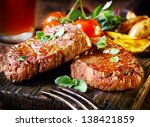 Succulent thick juicy portions of grilled fillet steak served with tomatoes and roast vegetables on an old wooden board