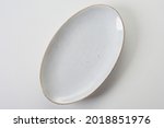 Top view of empty clean oval shaped white ceramic serving plate with golden rim on white background