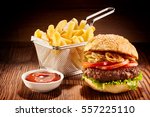 Studio shot of high burger with french fries in small fry basket and bowl of ketchup on wooden surface