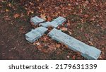 Devastated Shattered Stone Concrete Crucifix in Act of Religious Hatred and Persecution Left on Ground Amoung Withered Autumn Foliage Leaves
