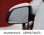 The mirror of the car is covered with snow.
Snow covered side view mirror of a black car.