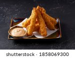 Tempura deep-fried EBI prawns with spiced sauce on a plate on a dark background. Appetizer in the style of Japanese cuisine. Deep-fried shrimp in breeding close-up. Horizontal photo.