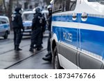 Small photo of German police car from berlin is in the focus and in the blurry background are several riot police cops standing on the street and waiting for action on a demonstration.