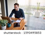 Young businessman sitting at a table at home working on a laptop and writing down ideas in a notebook