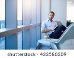 Portrait of a positive young businessman sitting in a modern corporate environment, looking at the camera while holding his diary, with gentle sunflare through the windows