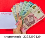 Small photo of Man holding a white envelope written of EMPLOYEE and new Indonesian banknotes. Usually, employees wages are given in an envelope with the words EMPLOYEE and are given at the beginning of the month.