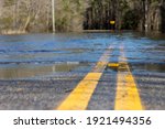 Small photo of Yellow dividing lines on an American road disappear into flood waters caused by a nearby river overtopping its banks after days of torrential rain.