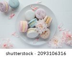 Beautiful colorful tasty macaroons and  white flowers  on a white tile background