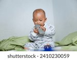 Small photo of The little Asian girl under 1 year old had just woken up and was sitting on the bed playing with the remote.