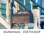 Black painted decorative mail box near front door with stairway and white banister or gaurd rails and green steps on home. House in the neighborhood or on the porch in a suburban area in yard.
