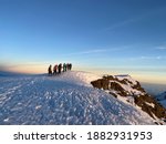 Group of hikers reaching the top of Kilimandjaro at sunrise with clear blue sky and walking on snow