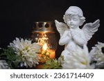 Angel, votive candle and flowers on black background