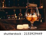 Small photo of Cigar, elegant glass of brandy on the bar counter. Alcoholic drinks, cognac, whiskey, port, brandy, rum, scotch, bourbon. Vintage wooden table in a pub at night.