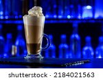 Cocktail layered baileys irish cream iced coffee on bar counter in a restaurant, pub. Drink with liqueur. Fresh prepared alcoholic cooler beverage at nightclub. Showcases, bottles, dark background.
