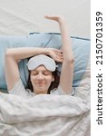 Small photo of woman in a sleep mask is lying in bed and yawning. a European woman with sleep problems and insomnia, waking up and falling asleep in a cozy house. sleep disorders or depression. healthy sleep and