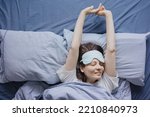 Small photo of top view of a woman in bed wearing a sleep mask, a happy European woman wakes up and stretches, does a warm-up, insomnia and sleep deprivation. the woman has had a good night's sleep and is resting