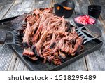 Traditional barbecue wagyu pulled beef offered with Carolina BBQ sauce and onion rings as closeup on an old rustic tray