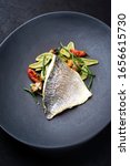 Small photo of Gourmet fried Italian gilthead fish filet with spinach pasta, glasswort and tomatoes as closeup on a modern design plate
