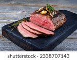 Small photo of Traditional Commonwealth Sunday roast with sliced cold cuts roast beef with garlic and salt as close-up on a rustic charred wooden board