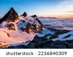 Sunrise Illuminates an Ocean of Clouds and Snowfield Peak as Two Small Climbers Ascend the Glacier Below. North Cascades National Park, Washington