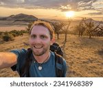 Small photo of Rana,Czech republic-July 12 2023:selfie of a paragliding pilot hiking to the Oblik hill with his paraglider backpack on his back in Ceske Stredohori mountains,with Rana hill in the background,Czechia