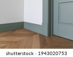 Fragment of classic interior with french herringbone parquet floor and green door and skirting boards. The final stage of finishing works in the apartment