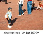 Small photo of Gubbio Umbria, Italy-May 15 2011; Boy with cap on backwards and backpack and people gather in European town square as sun lowers and shadows lengthen in late afternoon.