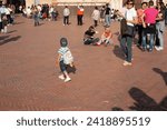 Small photo of Gubbio Umbria, Italy-May 15 2011; Boy with cap on backwards walks across European town square as sun lowers and shadows lengthen in late afternoon and people gather.