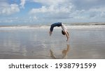 Small photo of gymnast girl doing a back handspring on the beach in the water