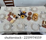 The top down view of a dining room table set for the holidays. There is fine china, a meat and cheese platter, corn muffins, Italian bread, and crackers.