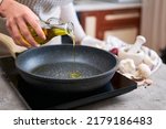 Woman pouring olive oil on frying pan at domestic kitchen
