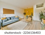 Small photo of a living room with wood flooring and yellow accent wall behind the sofa is a blue couch that sits on a white area rug