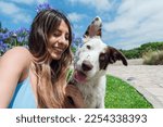 Small photo of portrait of border collie dog with white fur with brown and green eyes looking at the camera with a funny face next to his owner who is happy smiling and looking at him, with sky on background.