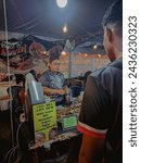 Small photo of Terengganu. February 11, 2024. Focus of an employee in a gray shirt serving customer orders at the Food Mania Festival. Night time atmosphere.
