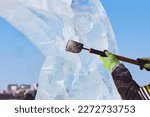 Small photo of An ice block is carved with a chisel in the hands of a sculptor on a sunny winter day. The master works with a homemade cutting tool. Close up.