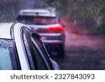Small photo of Heavy rain falls on the roof of a car during a thunderstorm. Red brake light in the dark. The concept of auto insurance and natural disasters. Driving on cloudy rainy days. Selective focus.