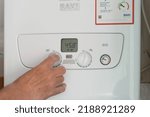 Small photo of Taken on 11 August 2022, Rossendale, Lancashire, UK. Man's hand turning down the dial on a gas boiler central heating system. Cost of utility bills soars.