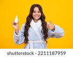 Small photo of Tunny nose and allergy, nasal spray. Teen girl in pajama use nasal drops, stuffed nose isolated on yellow background.