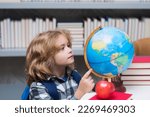 Pupil looking at globe in library at the elementary school. Nerd school kid. Clever child from elementary school with book. Smart genius intelligence kid ready to learn. World globe.